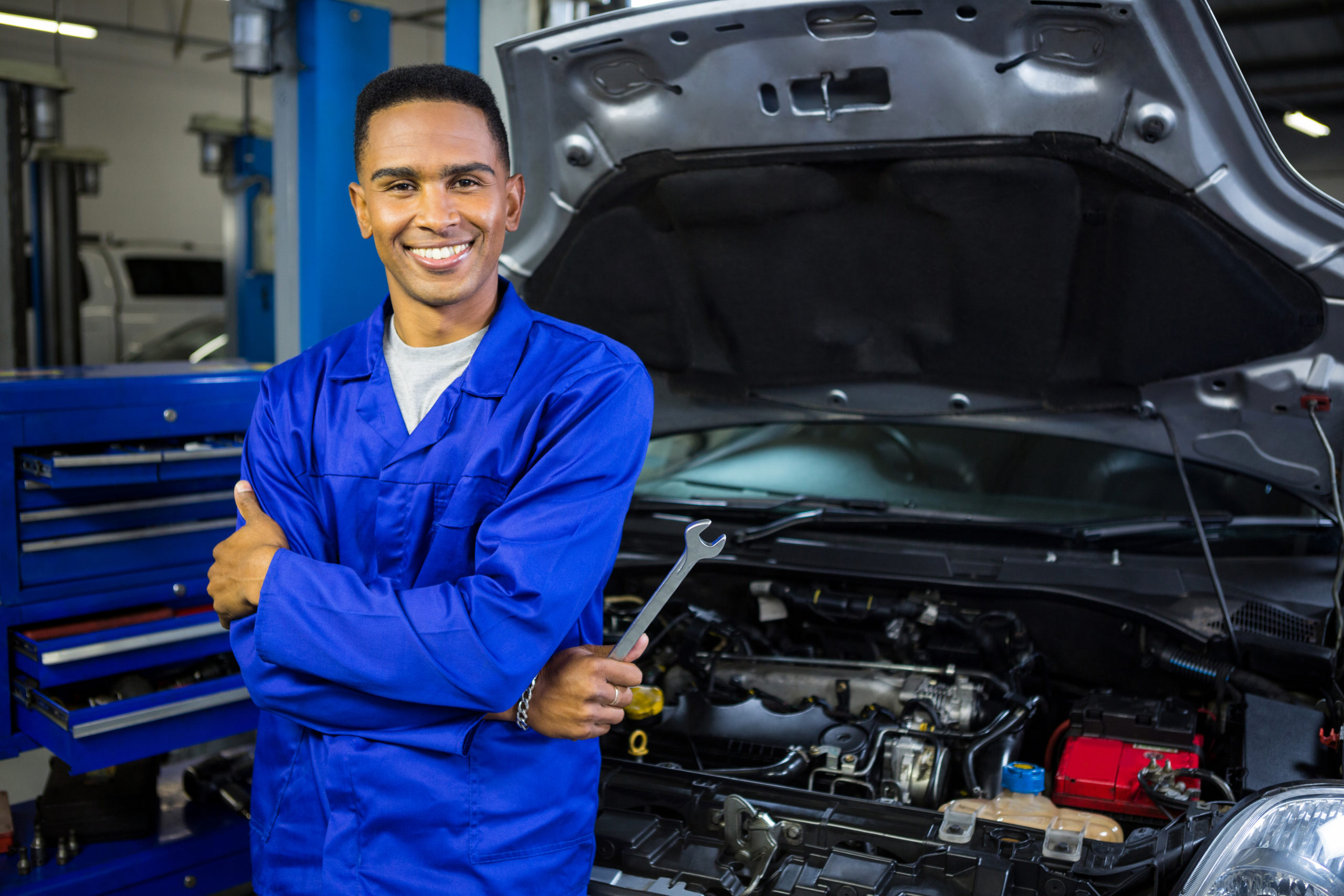 Smiling mechanic with arms crossed holding a spanner